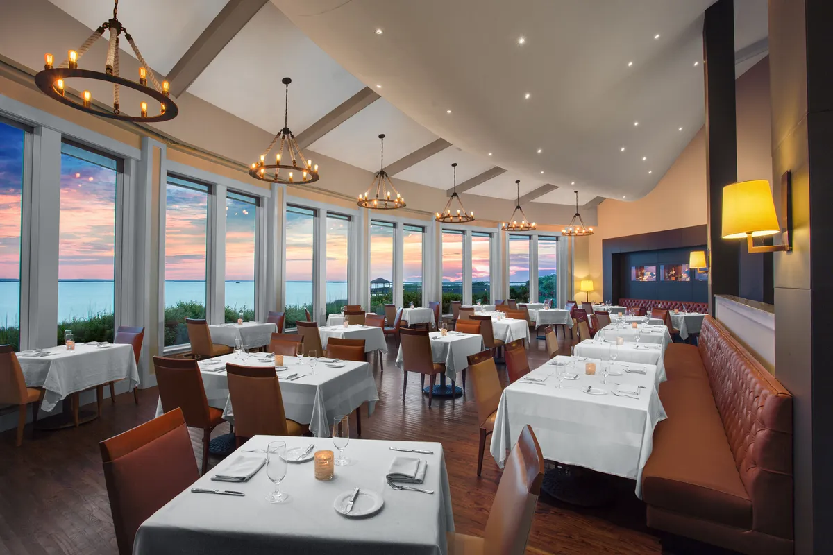 An elegantly set dining area featuring large windows with sunset views, cozy seating, and sophisticated lighting, creating a refined and inviting atmosphere for memorable meals.