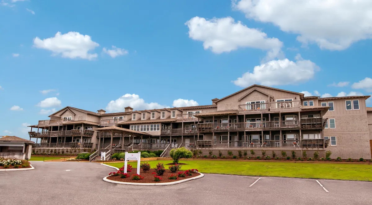 A multi-story building is highlighted with several balconies overlooking a landscaped garden. Outdoor seating areas provide a welcoming spot for guests to sit, sip coffee, or enjoy the scenery. The angle emphasizes the abundance of private balconies and the seamless transition from interior comfort to outdoor enjoyment.