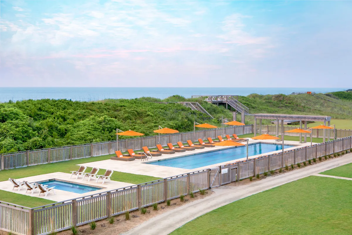 A serene poolside scene with orange umbrellas, lounge chairs, and a stunning ocean view in the background. Guests can be seen relaxing and enjoying the peaceful ambiance.