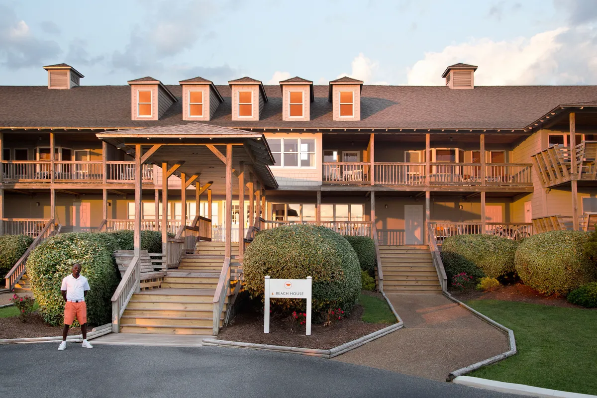 The inviting front porch of the property features comfortable seating surrounded by lush bushes and greenery. The soft glow of sunset adds warmth to the scene, suggesting a peaceful place to relax, dine outdoors, or socialize in the evening. The staircase and signage make this a welcoming entrance that blurs the line between indoors and out.